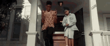 a man and a woman are standing on the porch of a house with the number 1226 on it .