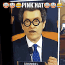 a man in a suit and tie is giving a speech in front of a sign that says ' pink hat '