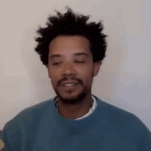 a man with a beard and curly hair is wearing a blue sweater and smiling with his eyes closed .