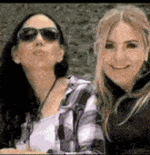 two women wearing sunglasses and plaid shirts are posing for a picture together .