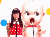 a woman is singing into a microphone while standing next to a baby doll .