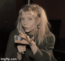 a girl with blonde hair is holding a microphone and making a face .