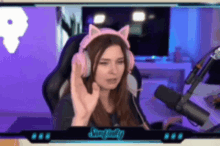 a woman wearing pink cat ears is sitting in front of a microphone .
