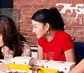 a woman in a red shirt is sitting at a table with boxes of pizza .