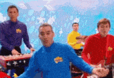 a group of men are playing instruments and one of them is wearing a blue shirt with the word wiggle on it .