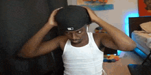 a man wearing a hat and a white tank top is adjusting his hat .