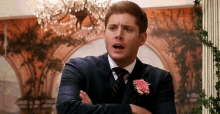 a man in a suit and tie is standing with his arms crossed and making a funny face .