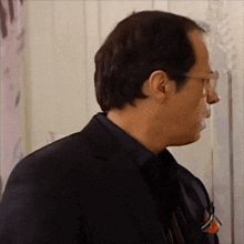 a man wearing glasses and a black suit is looking at something .