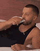a shirtless man is brushing his teeth in bed .