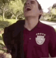 a man in a maroon shirt is laughing with his mouth wide open .