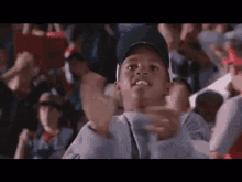 a young boy wearing a baseball cap is standing in a crowd of people watching a baseball game .