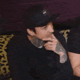 a man wearing a huf hat is sitting on a couch with his hand on his chin .