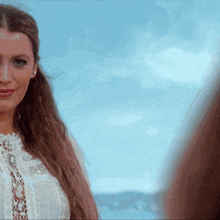 a woman in a white lace top looks at the camera