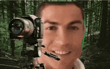 a man is smiling while holding a camera in front of his face in the woods .