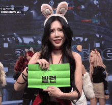 a woman wearing bunny ears is holding a green piece of paper with korean writing on it
