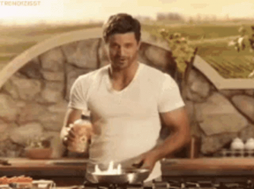 a man in a white t-shirt is cooking on a stove