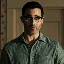 a man wearing glasses and a gray shirt looks at the camera