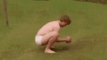 a shirtless man in a diaper is squatting down in the grass .