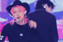a man with pink hair is wearing a black hat and headphones while standing next to another man .