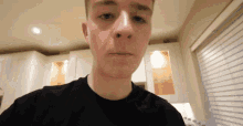 a young man in a black shirt looks at the camera in a kitchen