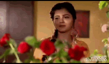 a woman is standing in front of a bunch of red roses and looking at them .