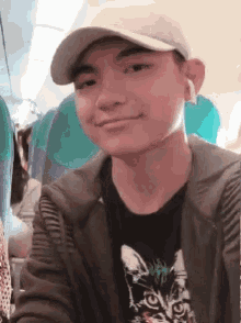 a young man wearing a hat and a cat t-shirt smiles while sitting on an airplane