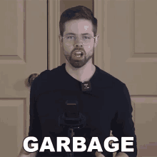 a man wearing glasses and a black shirt is holding a microphone and says garbage