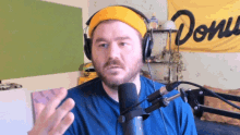 a man wearing headphones and a yellow headband stands in front of a microphone in front of a banner that says done