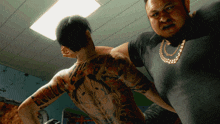 a man with a tattoo on his back stands next to another man with a necklace
