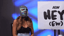 a woman wearing a mask is sitting in front of a sign that says hey ( ew )