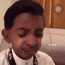 a young boy is making a funny face while wearing a camera strap around his neck .