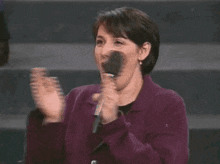 a woman in a purple jacket is holding a microphone in her hand