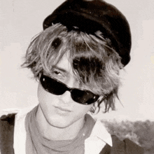 a black and white photo of a young man wearing a hat and sunglasses .