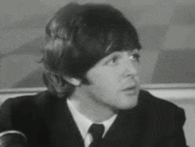 a black and white photo of a man in a suit and tie talking into a microphone