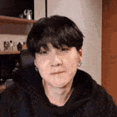 a close up of a person wearing a black hoodie and earrings making a funny face .