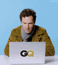 a man sitting in front of a laptop with the gq logo on it