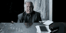 an older man is sitting at a desk with a broken glass table .