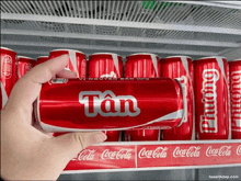 a hand is holding a red can of tan coca cola