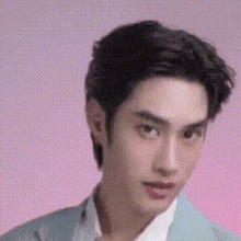 a close up of a man 's face with a pink background . he is wearing a blue jacket and white shirt .