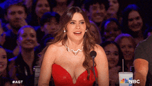 a woman in a red dress stands in front of a microphone and a cup that says nbc on it