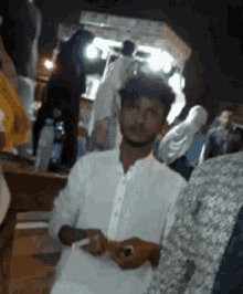 a man in a white shirt is smoking a cigarette in a crowd of people .