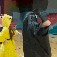 a man in a black robe is standing next to a girl in a yellow hoodie