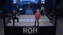 a man in a pink jacket is standing in a wrestling ring with a sign that says roh