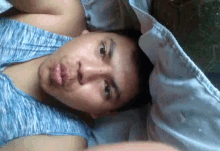 a man in a blue tank top is laying on a bed and making a face