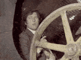 a man in a suit is holding a gun behind a large wheel
