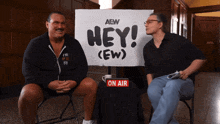 two men are sitting in front of a sign that says hey ( ew )
