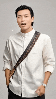 a man wearing a white shirt with a black strap around his shoulder