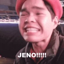 a man wearing a red hat is making a funny face with the word jeno written on the bottom of his face .