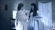two women in white dresses are standing next to each other in a bedroom .