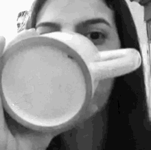 a black and white photo of a woman drinking from a coffee cup